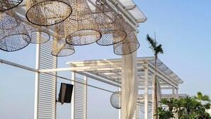 An outdoor seating area with tables and chairs, a pergola structure, and a view of the cityscape.