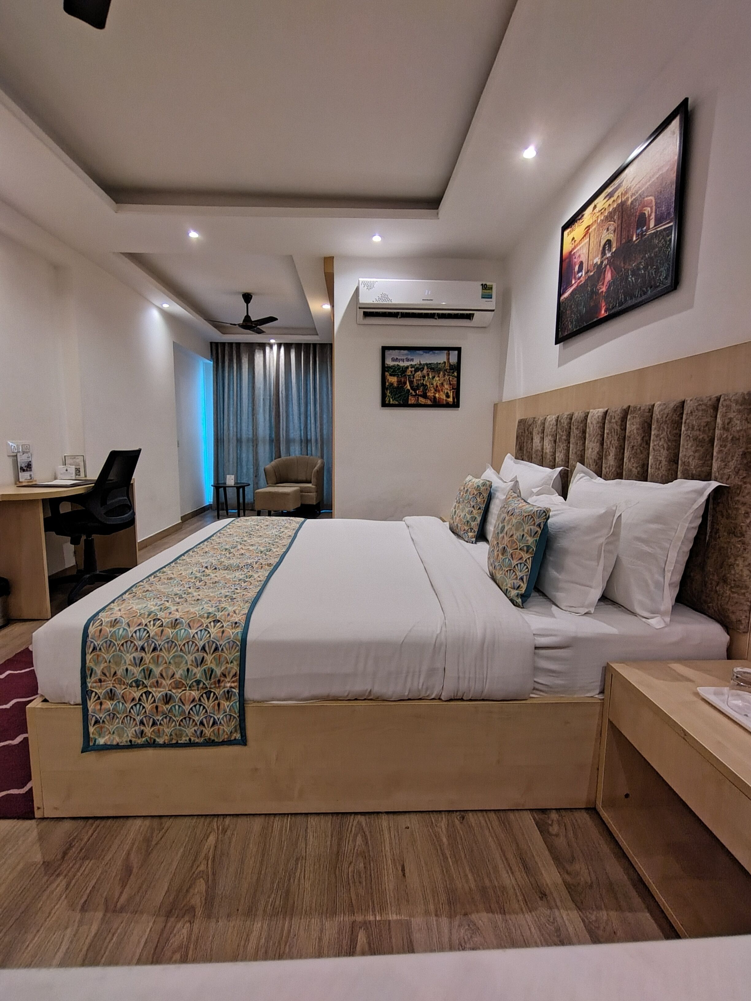 Een moderne hotelkamer met een groot bed, een bureau, een stoel, een airconditioner en een schilderij aan de muur.