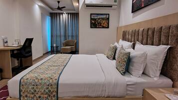 Een moderne hotelkamer met een groot bed, een bureau, een stoel, een airconditioner en een schilderij aan de muur.