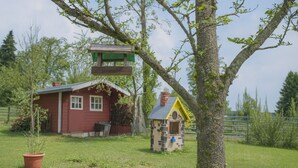A red wooden house with a small attached structure, a tree with a swing, and a fenced area.