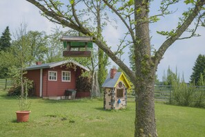 Ein rotes Holzhaus mit einem kleinen Anbau, ein Baum mit einer Schaukel und einem eingezäunten Bereich.