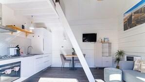 A modern kitchen with a dining area, a TV mounted on the wall, and a sofa in the living space.