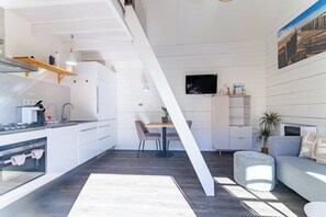 A modern kitchen with a dining area, a TV mounted on the wall, and a sofa in the living space.