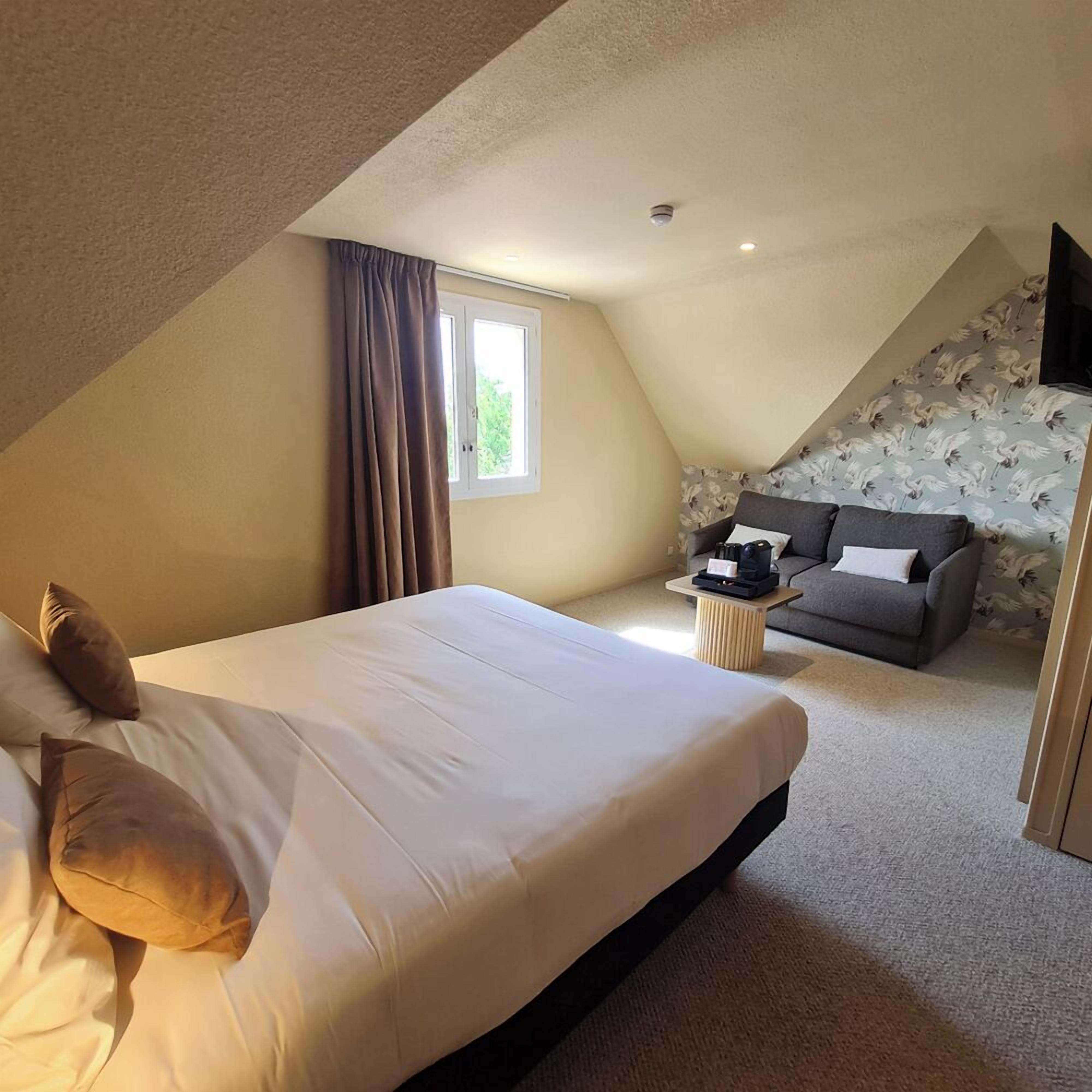 A bedroom with a large bed, a sofa, a small table, and a window.