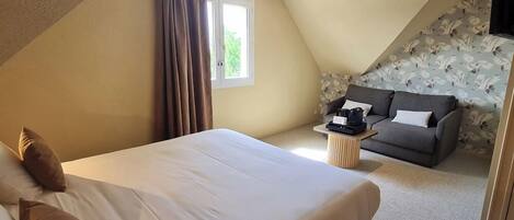 A bedroom with a large bed, a sofa, a small table, and a window.