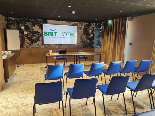 A conference room with a large screen displaying "BRIT HOTEL ALENÇON" and a row of blue chairs facing the screen. - BRIT HOTEL CONFORT ALENCON (Alencon)