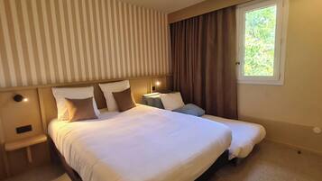 Une chambre d’hôtel avec un grand lit, une table de chevet, une commode, une fenêtre avec des rideaux et un mur à rayures.