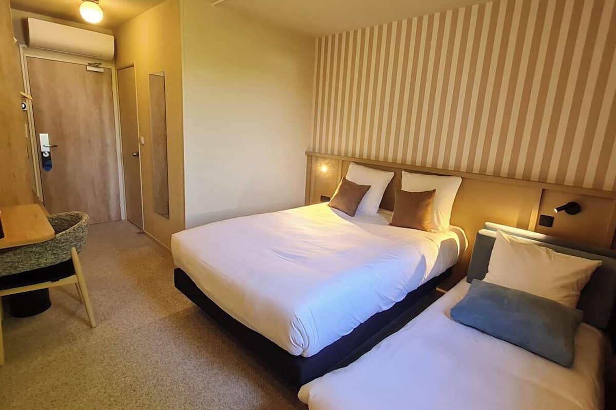 A hotel room with two beds, a desk, and a striped wall.