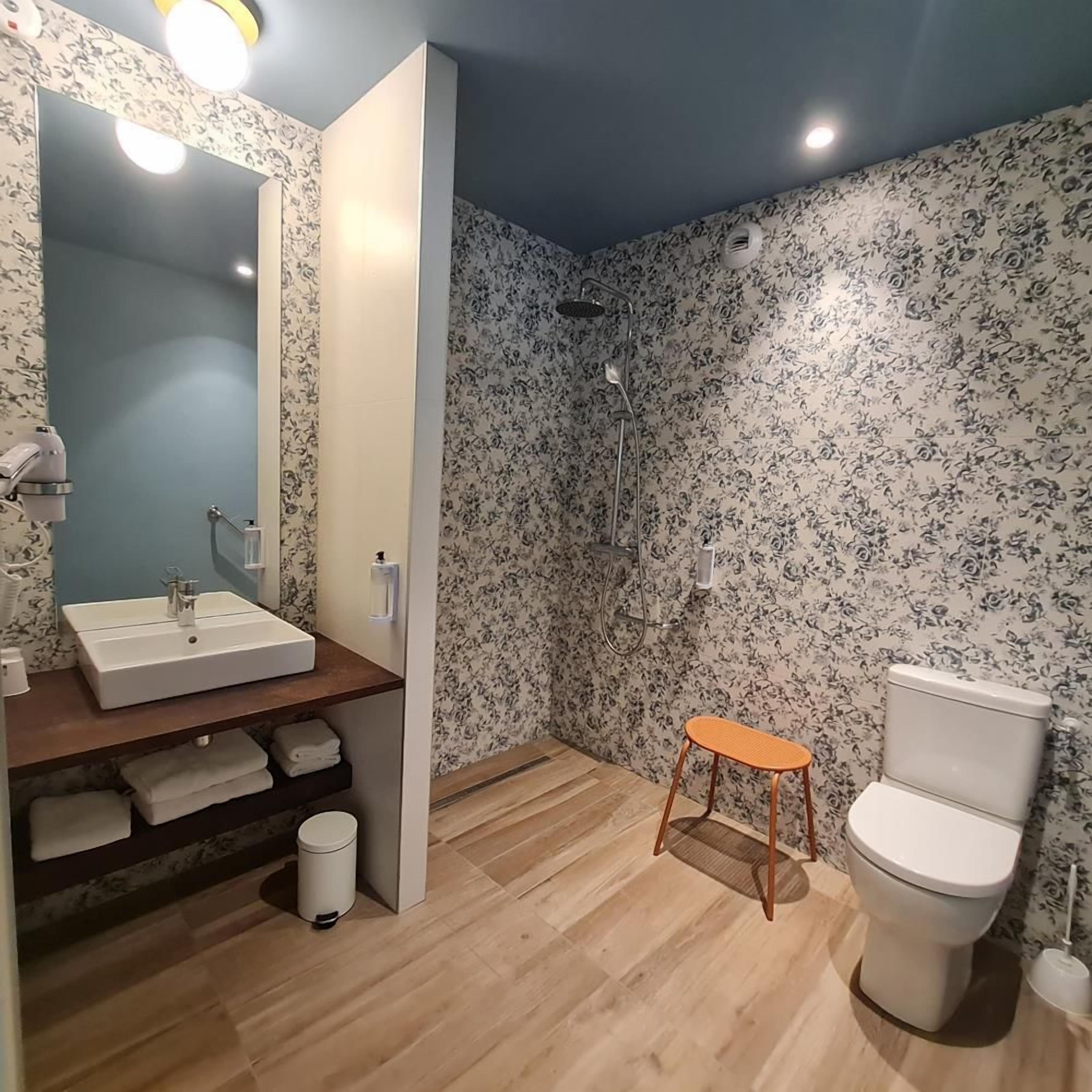 Een badkamer met een wastafel, toilet, douche en een klein krukje.