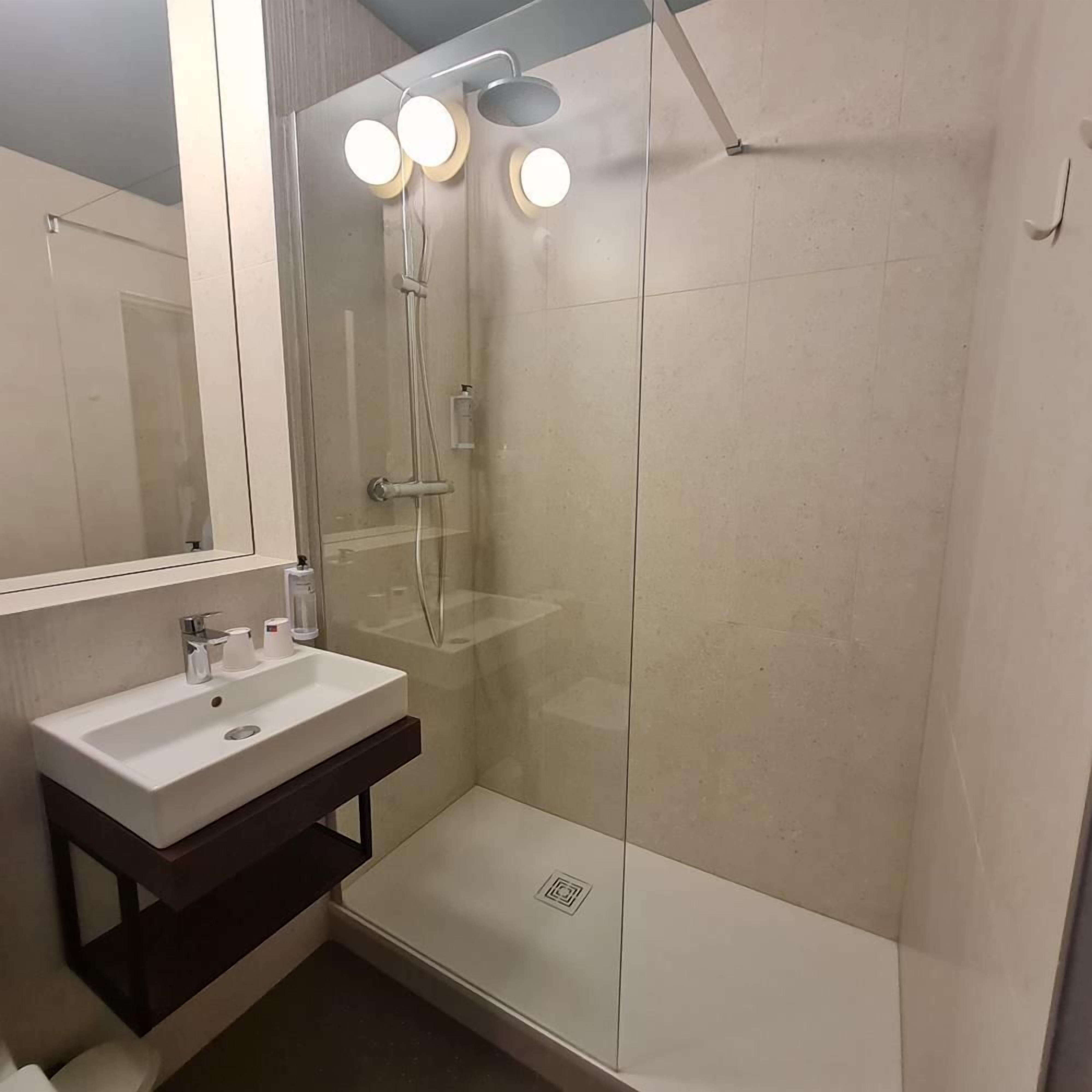 A modern bathroom with a glass-enclosed shower, a white sink, and a mirror above it.