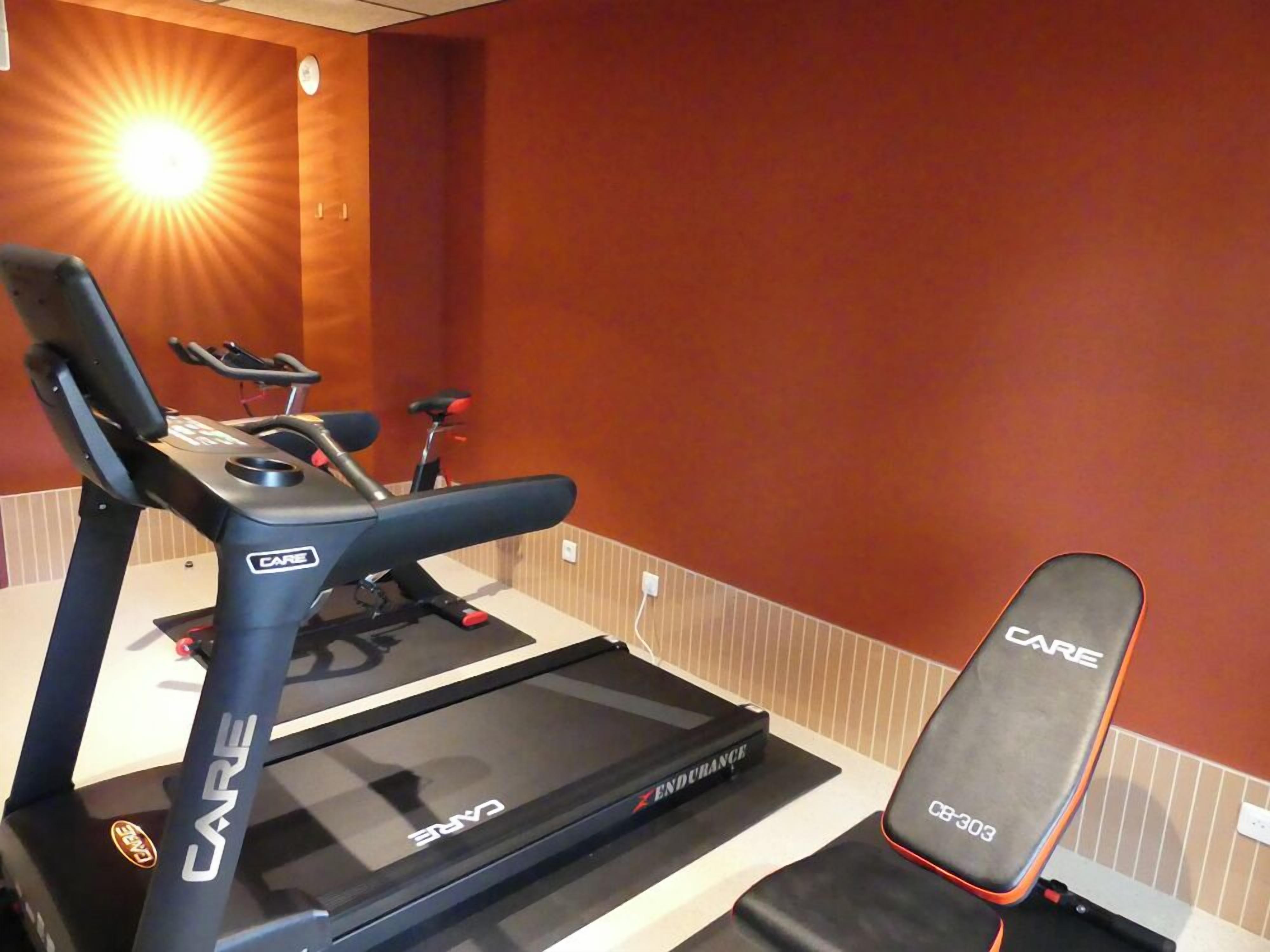 A treadmill and a bench in a room with a red wall and a sunlit corner.