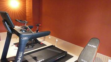 A treadmill and a bench in a room with a red wall and a sunlit corner.
