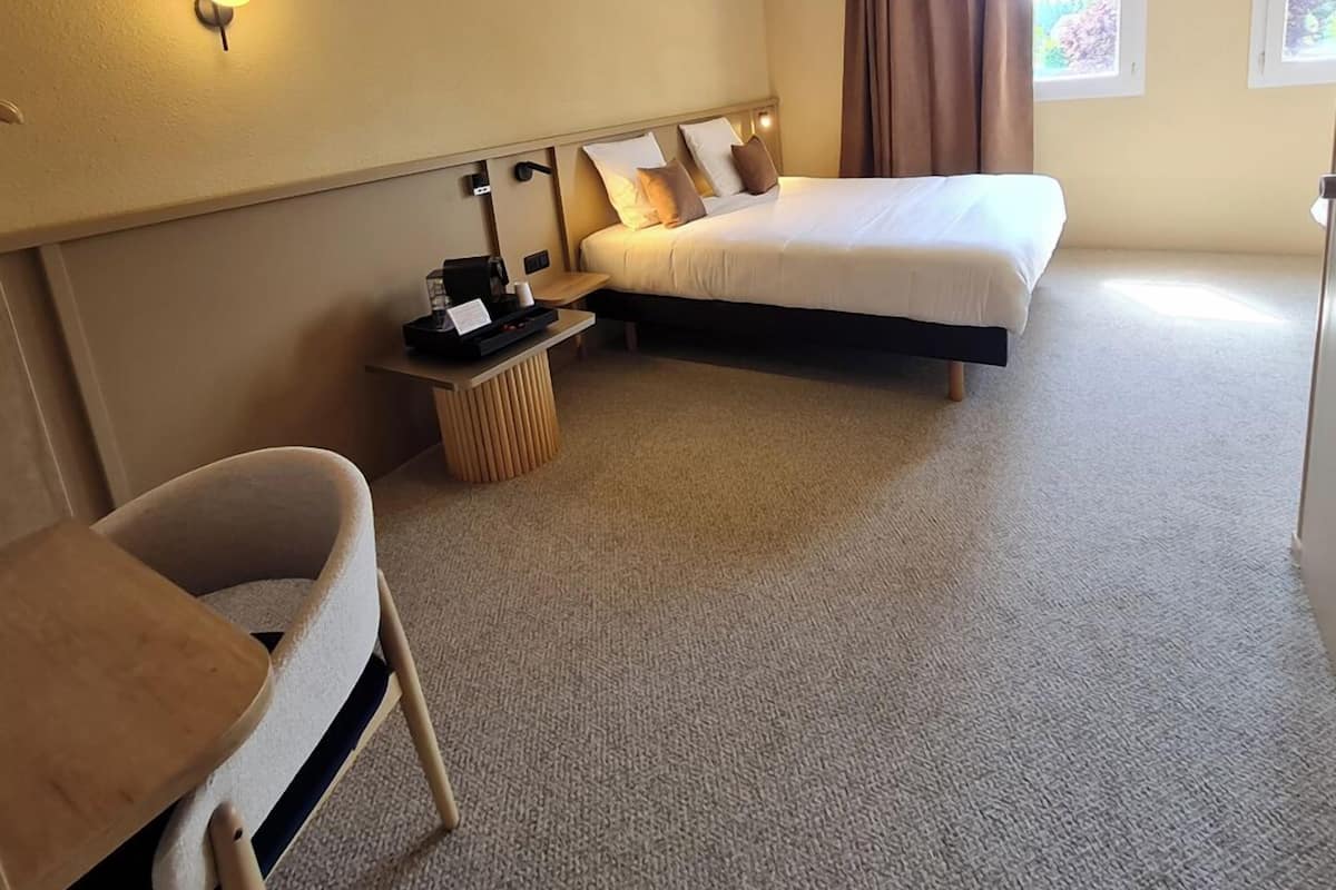 A hotel room with a bed, a desk, a chair, and a window with curtains.