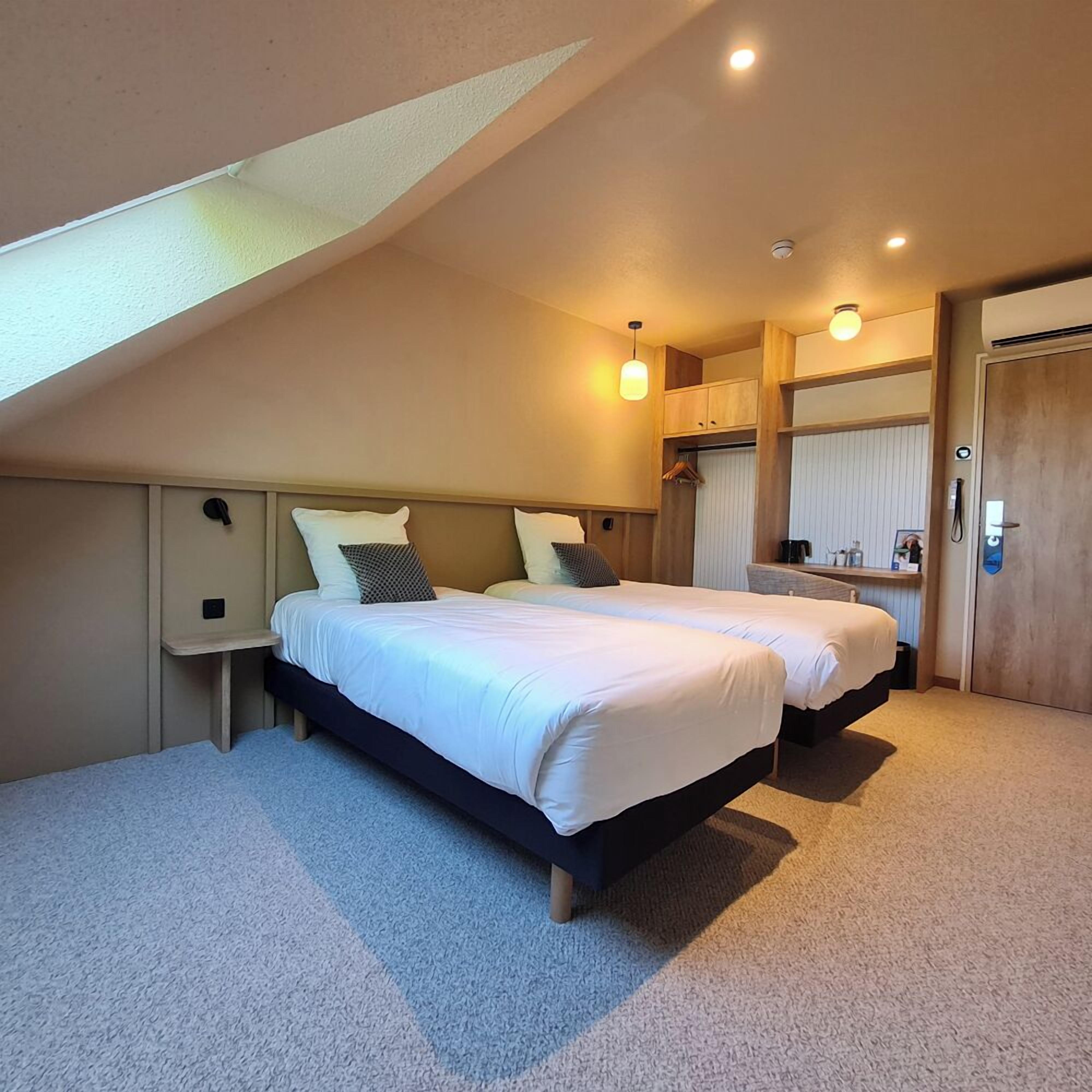 A bedroom with two beds, a skylight, a wardrobe, and a bedside table.
