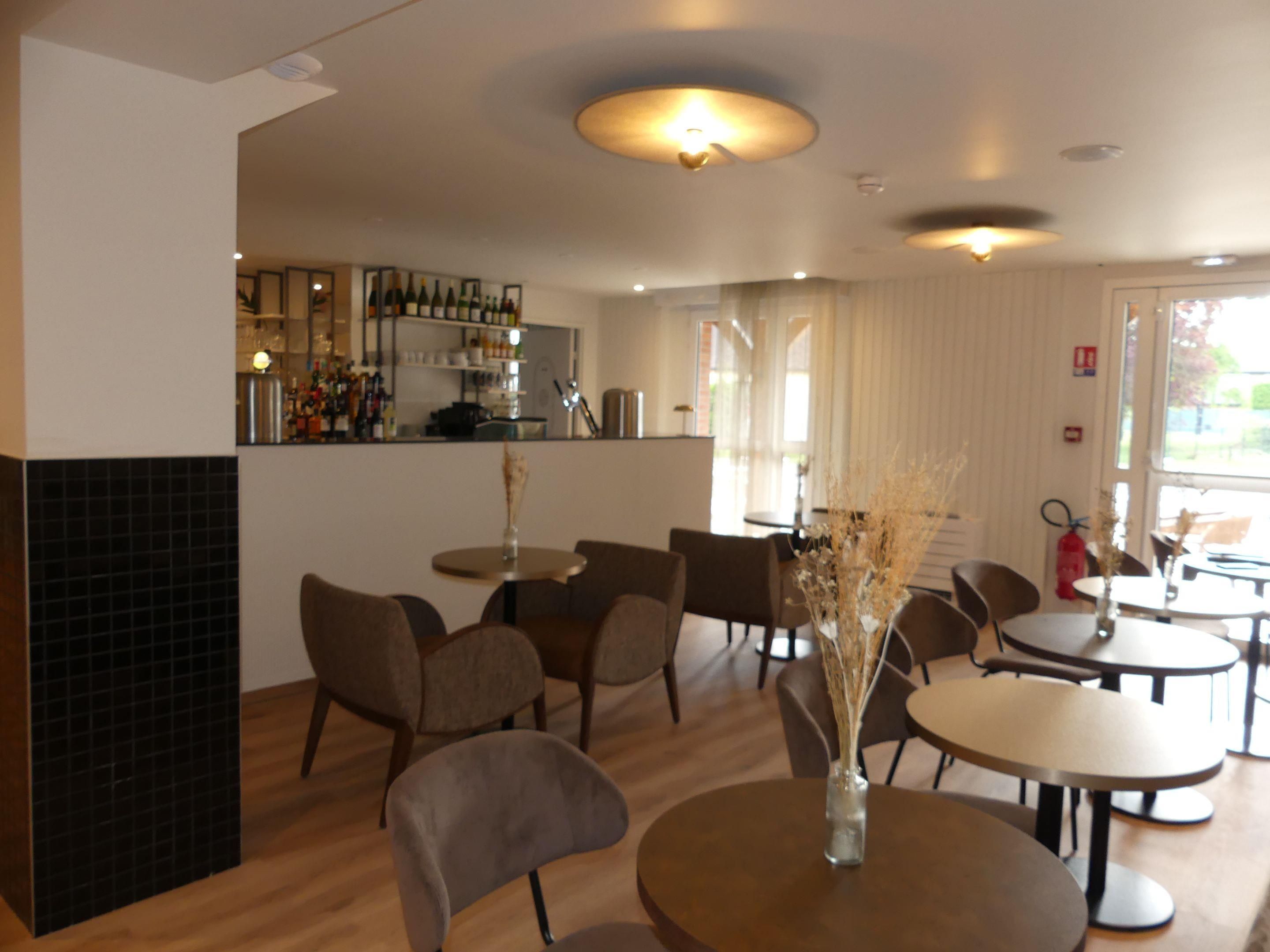 A restaurant interior with round tables, chairs, a bar area, and a view of the outdoors.