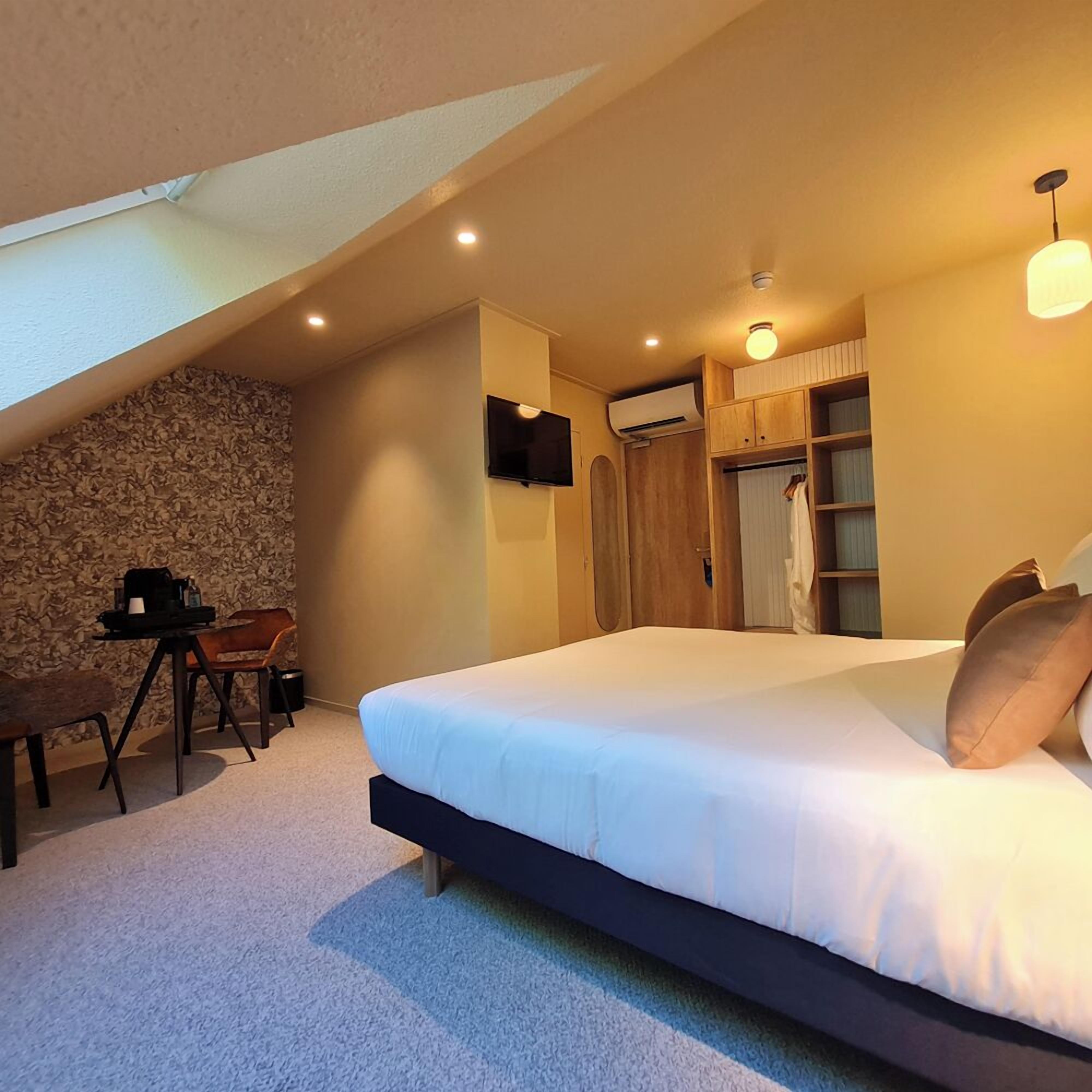 A bedroom with a large bed, a desk with a chair, a stone wall, and a wardrobe.