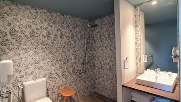 A bathroom with a toilet, a shower, and a sink with a mirror.