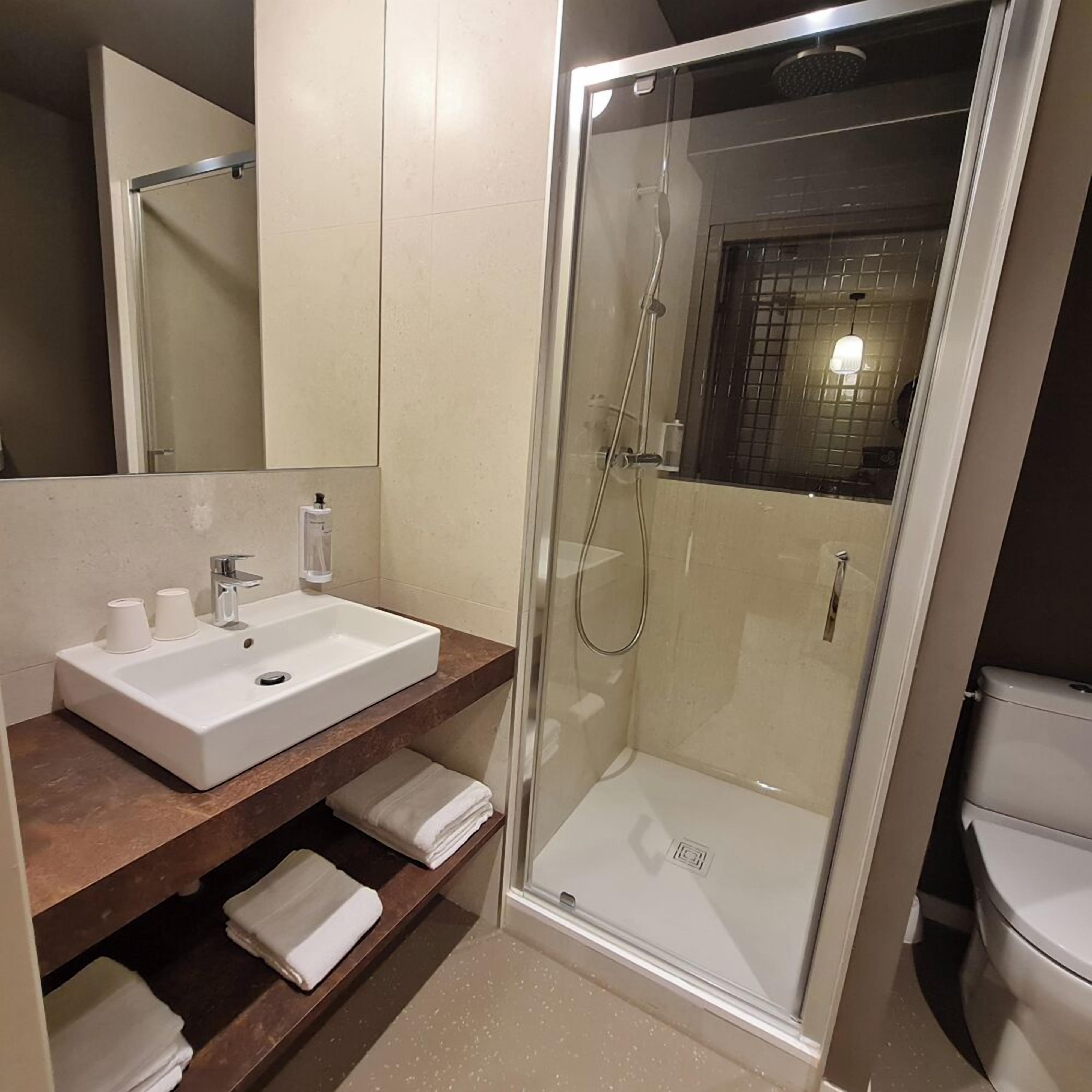 Et moderne badeværelse med et glasafskærmet brusebad, en hvid vask og et spejl over vasken.