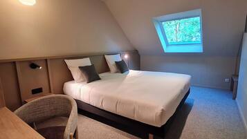 Een slaapkamer met een bed, een klein tafeltje, een stoel, een dakraam en een plafondlamp.