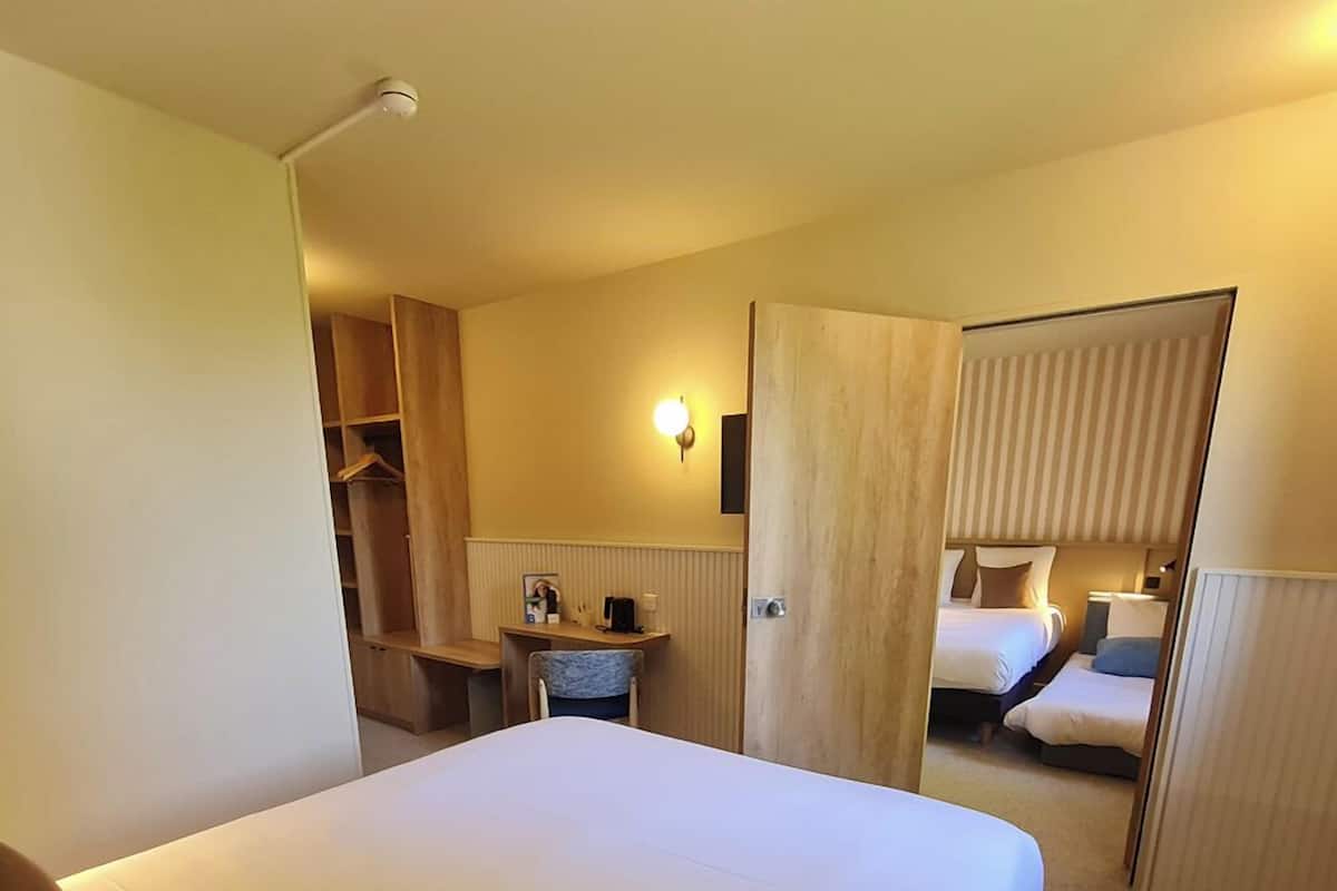 A hotel room with a large bed, a desk with a chair, a wardrobe, and a bathroom visible through an open door.