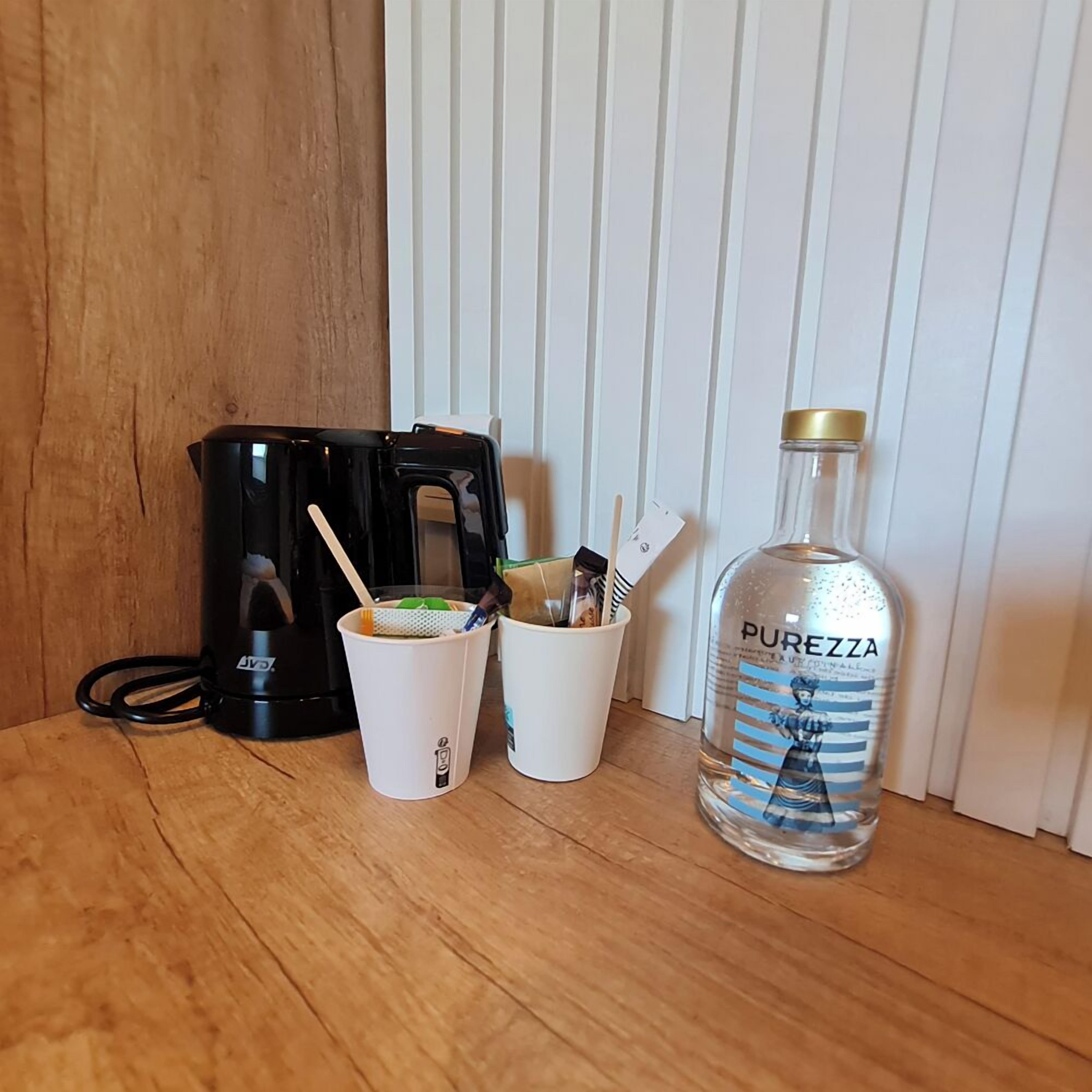 Una cafetera, dos tazas y una botella de agua Purezza sobre una superficie de madera.