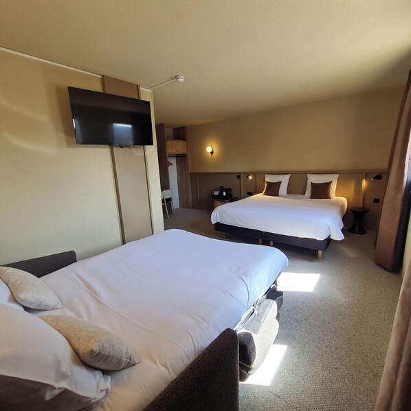 Une chambre d’hôtel avec deux lits, un téléviseur à écran plat fixé au mur et une table de chevet avec une lampe.