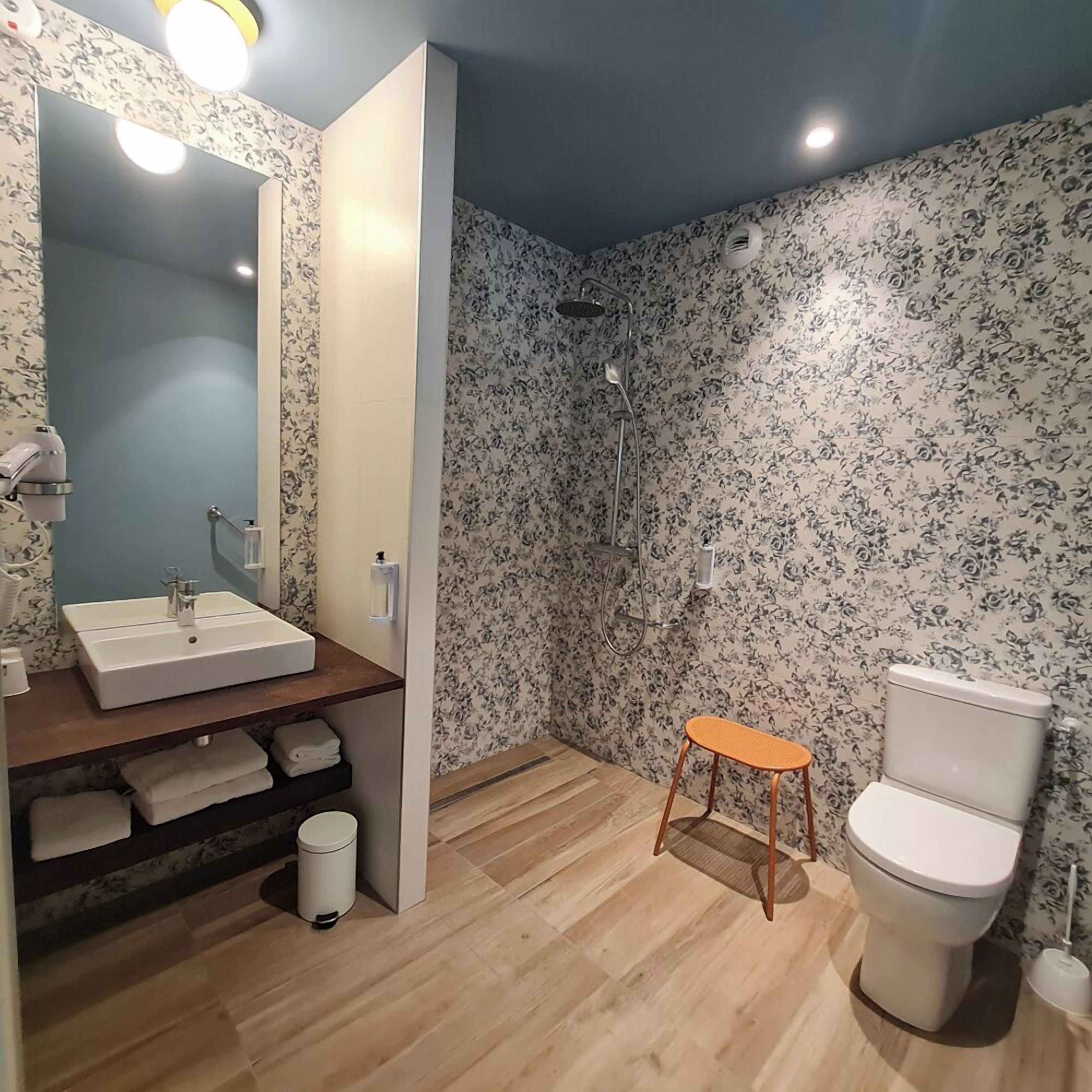 Un baño con lavamanos, inodoro, ducha y un taburete pequeño.
