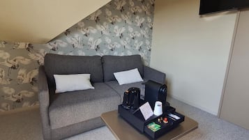 A room with a grey sofa, a coffee table with a kettle, and a flat-screen TV mounted on the wall.