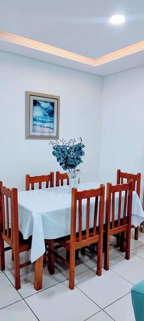 A dining area with a round table, wooden chairs, a vase with blue flowers, and a framed picture on the wall. - Guarujá Sol e Praia (Guarujá)