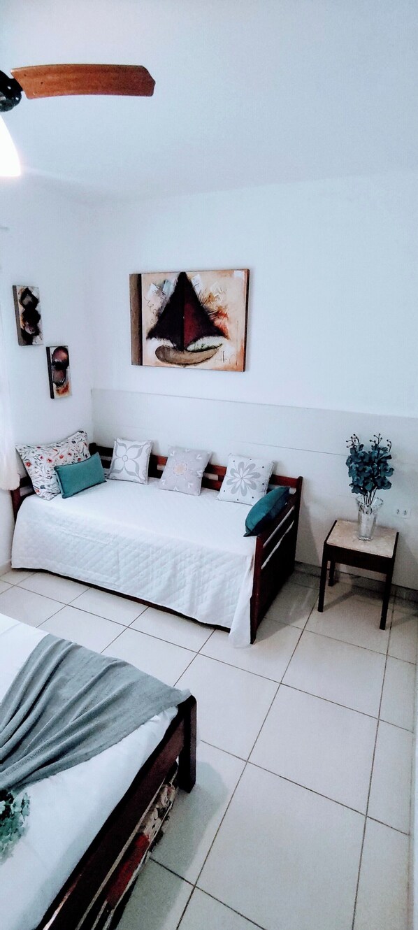 A bedroom with a bed, a bedside table, a chair, and a painting on the wall. - Guarujá Sol e Praia (Guarujá)