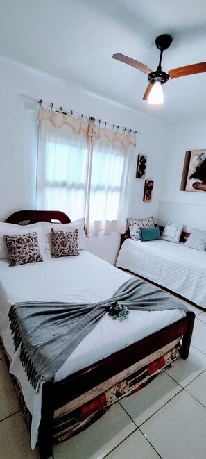 A bedroom with a large bed, a ceiling fan, and a window with curtains. - Guarujá Sol e Praia (Guarujá)