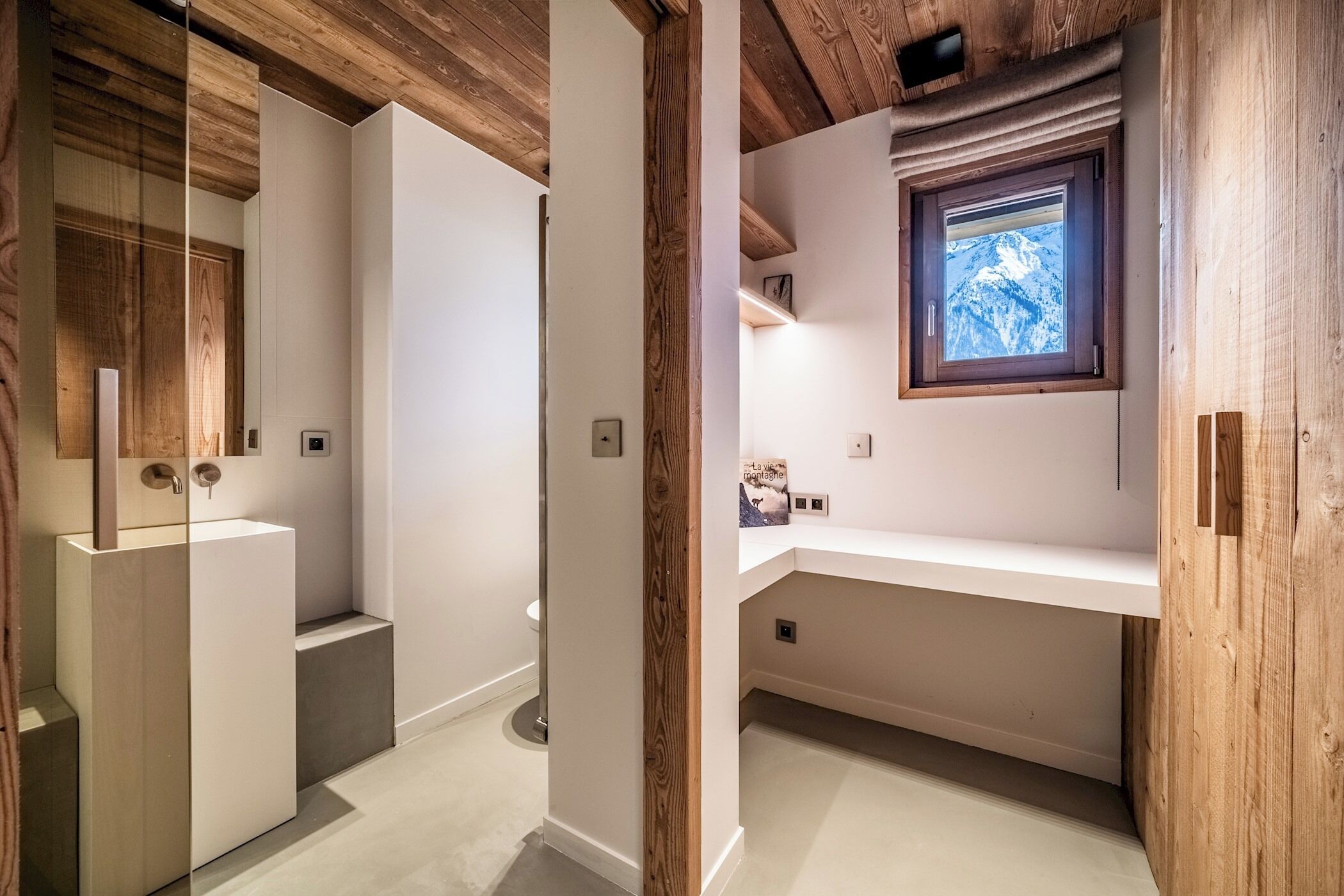 A modern bathroom with a wooden ceiling, a built-in sink, and a window with a mountain view.
