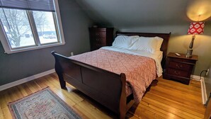 Une chambre à coucher avec un lit en bois, une table de chevet, une lampe, une fenêtre et un tapis.