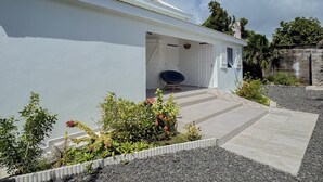 A modern white building with a covered patio area, a stone wall, and a variety of plants. - Villa Fleur de Sel with swimming pool 5 minutes walk from the beach (le gosier)