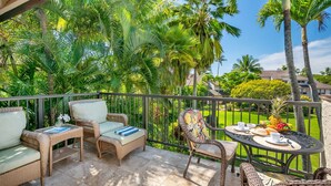 Ein Balkon mit Korbmöbeln, einem Tisch für zwei Personen und Blick auf einen gepflegten Garten und ein Haus.