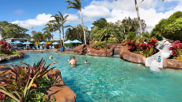 Ein klares Schwimmbecken mit Wasserrutsche, umgeben von Palmen und tropischer Bepflanzung.