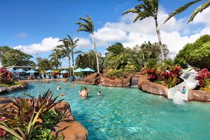 Una piscina cristalina con un tobogán de agua, rodeada de palmeras y plantas tropicales.