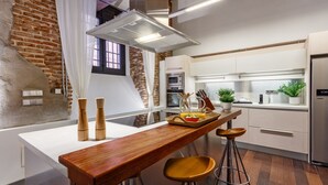 A modern kitchen with a wooden bar counter, stools, and a brick wall. - Historic Loft for 7 in Heart of Madrid (Madrid)