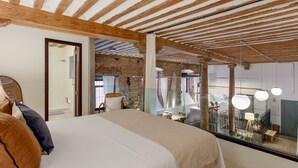 A bedroom with a large bed, a wooden ceiling, and a view of a dining area. - Historic Loft for 7 in Heart of Madrid (Madrid)