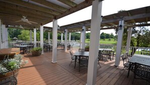 Un patio al aire libre con piso de madera, columnas blancas y mesas y sillas.