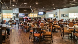Un restaurante con varias mesas y sillas, una zona de bar y una pantalla de televisión.