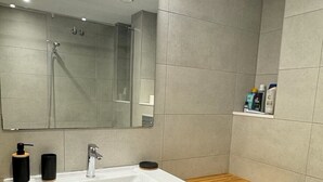 Un bagno moderno con un lavandino bianco capiente, un piano d'appoggio in legno, uno specchio e un box doccia.