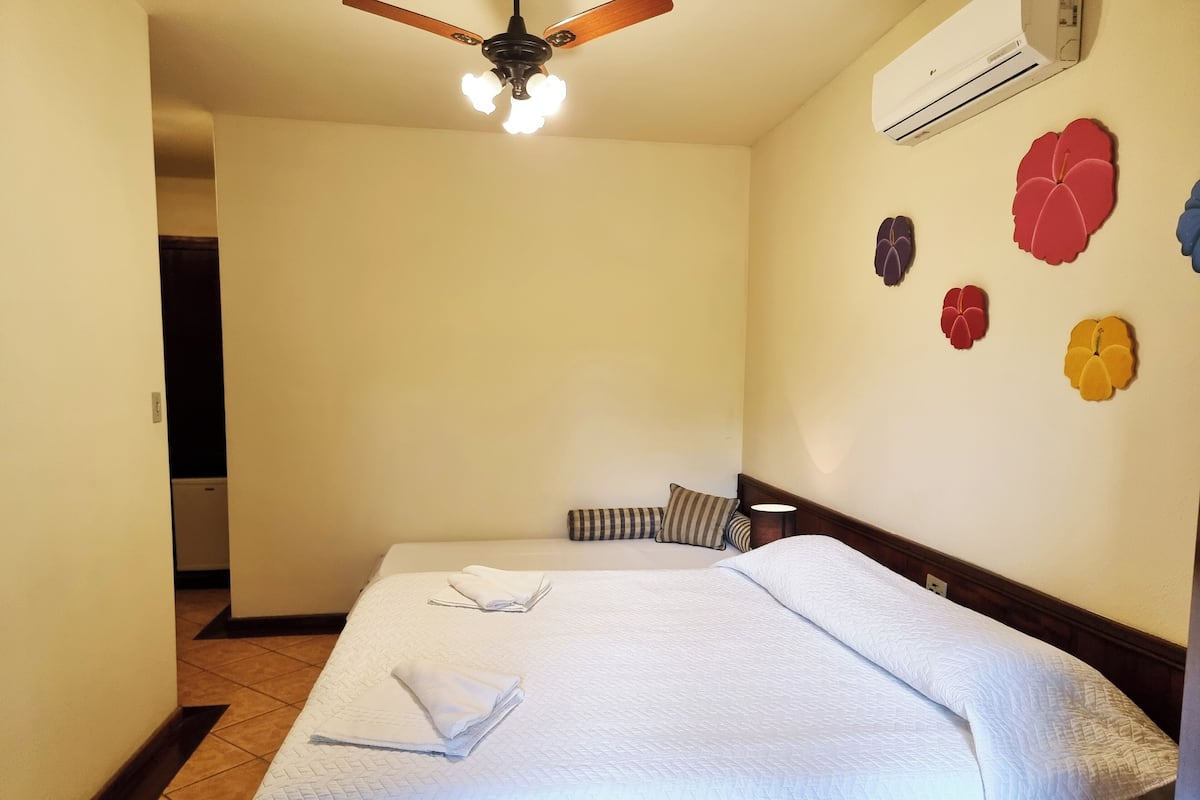 Quarto de hotel com cama, ventilador de teto, ar condicionado e decoração na parede.