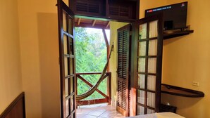 A room with a bed, a TV on a shelf, and a view of greenery outside. - Vale do Sonho Hotel e Eventos (Guararema)