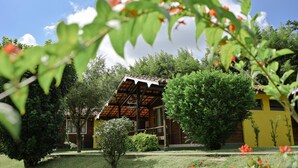 A rustic wooden house with a yellow facade, surrounded by lush greenery and a clear blue sky. - Vale do Sonho Hotel e Eventos (Guararema)