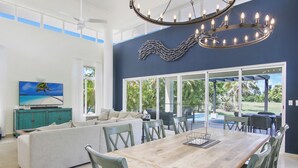 A spacious living room with a large wooden dining table, comfortable seating, a television, and a view of the outdoors. - Golf Villa in Bavaro - Pool, Jacuzzi, Staff (Punta Cana)