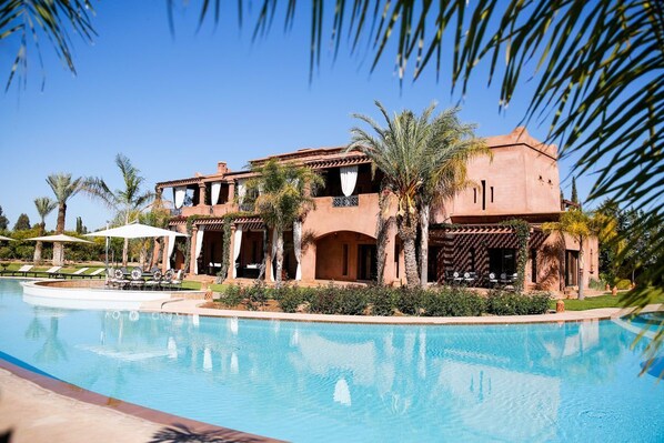 A resort with a swimming pool, palm trees, and a building with a terracotta facade. - Villa Abbas - Six Bedroom Villa, Sleeps 12 (Chaibate)