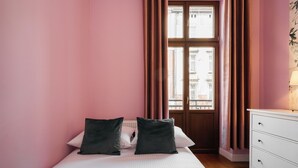 Een slaapkamer met een bed, twee kussens, een dressoir en een raam met gordijnen.