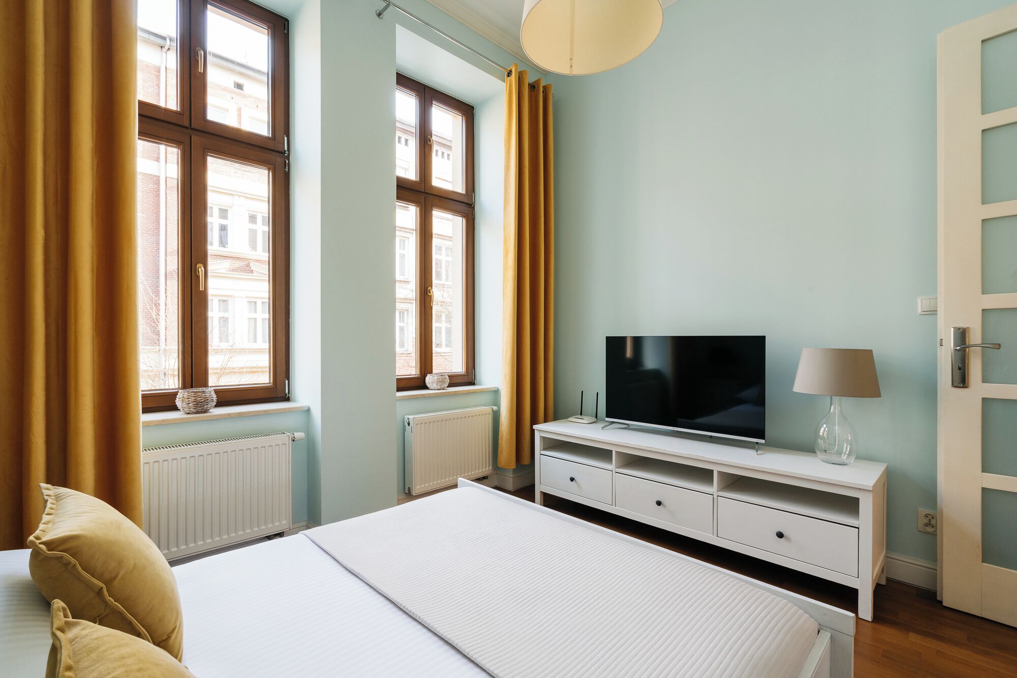 Une chambre à coucher avec un lit, une télévision, une lampe et une fenêtre avec des rideaux.