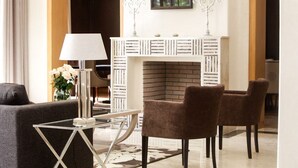 A modern living room with a glass coffee table, two brown armchairs, a white fireplace, and a candelabra.